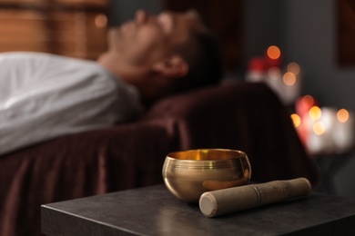 Photo of Man at healing session in dark room, focus on singing bowl