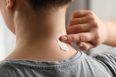 Photo of Woman applying ointment onto her neck indoors, closeup