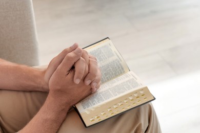 Religious man with Bible praying indoors, closeup