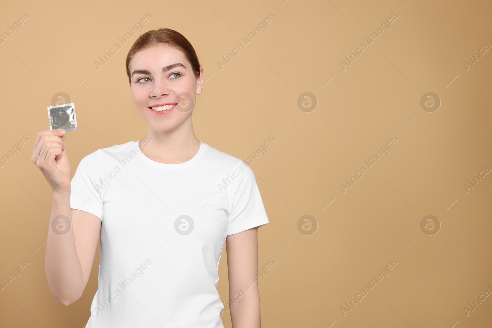 Photo of Woman holding condom on beige background, space for text. Safe sex