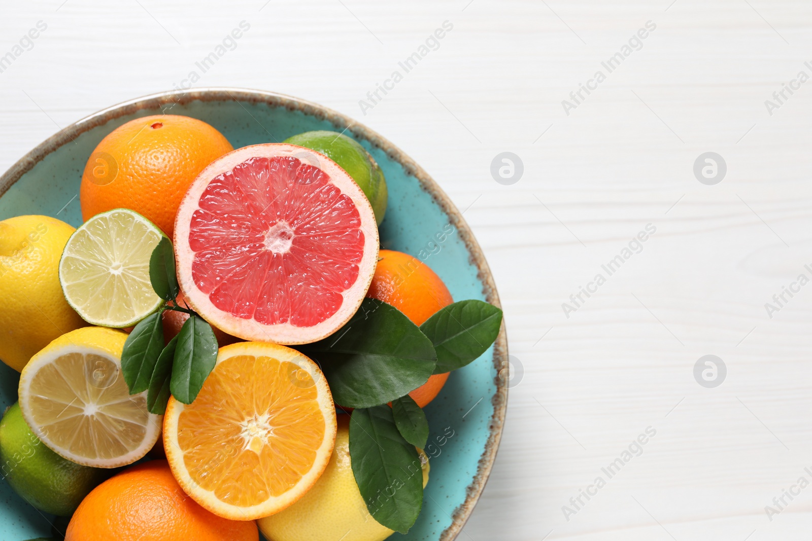 Photo of Different cut and whole citrus fruits on white wooden table, top view. Space for text