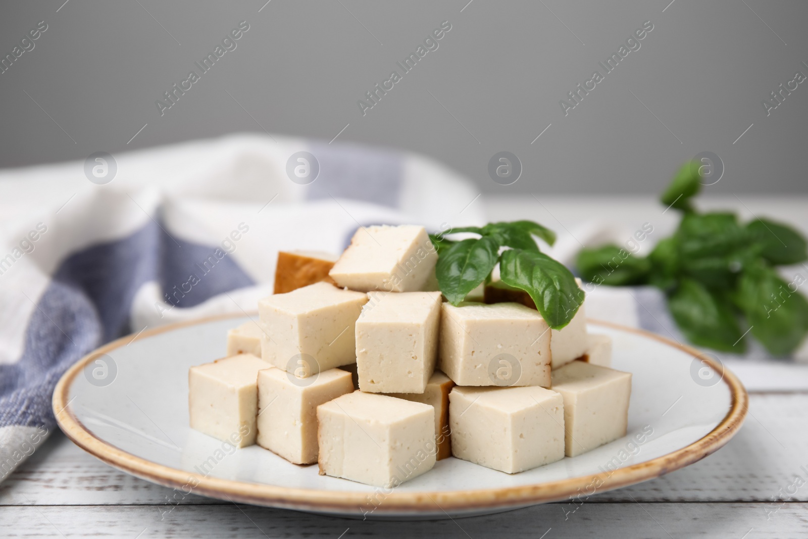 Photo of Plate with delicious smoked tofu and basil on white wooden table, closeup