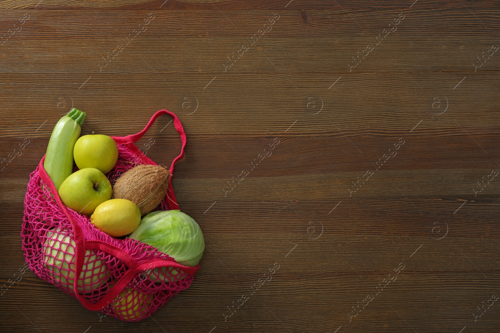 Photo of Net bag with vegetables and fruits on wooden table, top view. Space for text