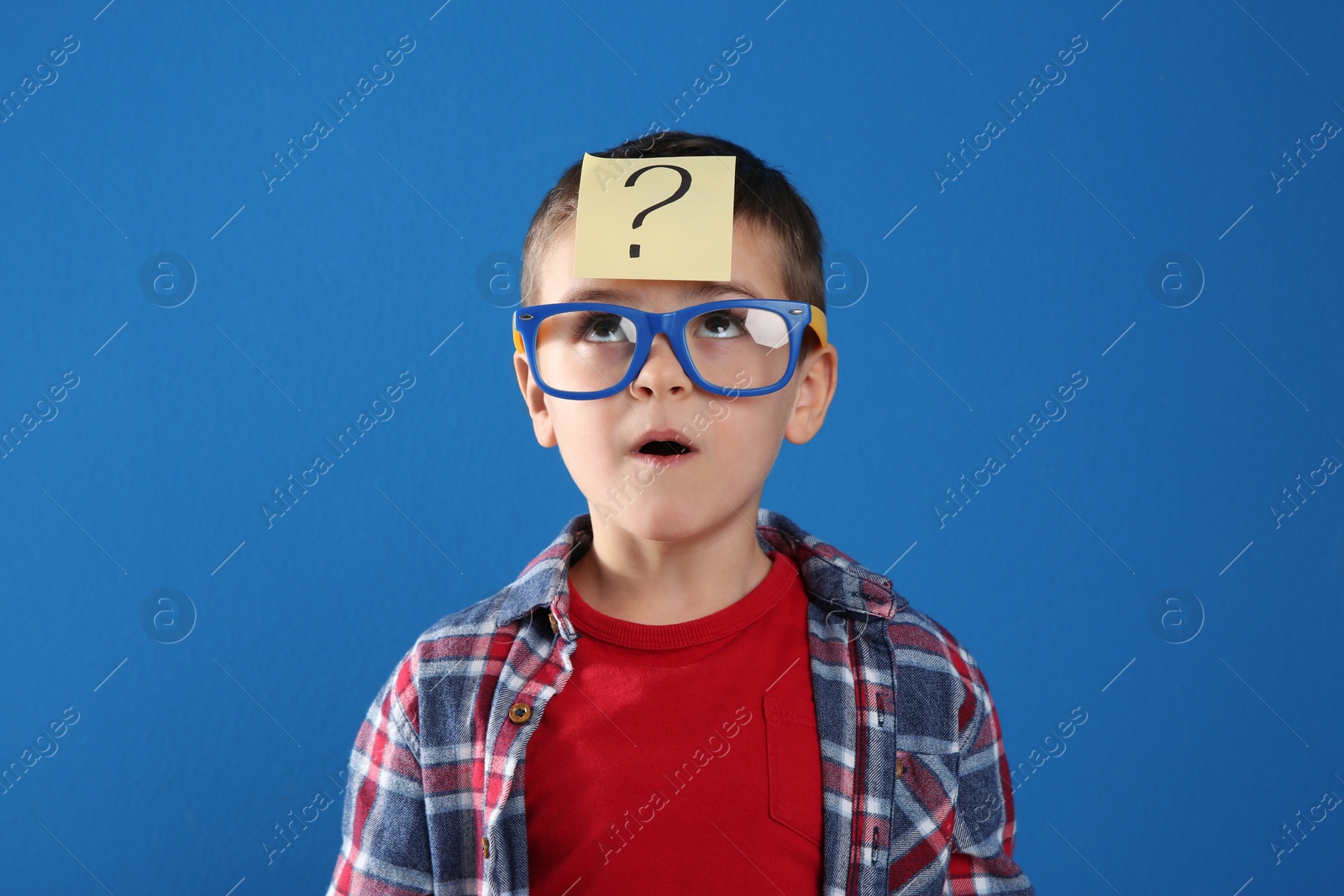 Photo of Emotional little boy with question mark on blue background