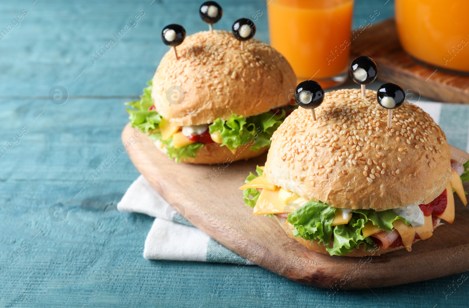 Photo of Cute monster burgers served on blue wooden table. Halloween party food