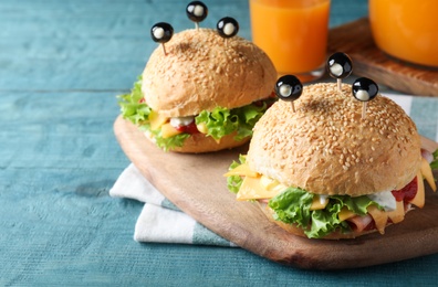 Photo of Cute monster burgers served on blue wooden table. Halloween party food