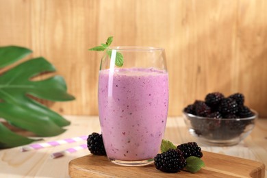 Photo of Delicious blackberry smoothie in glass and berries on wooden table