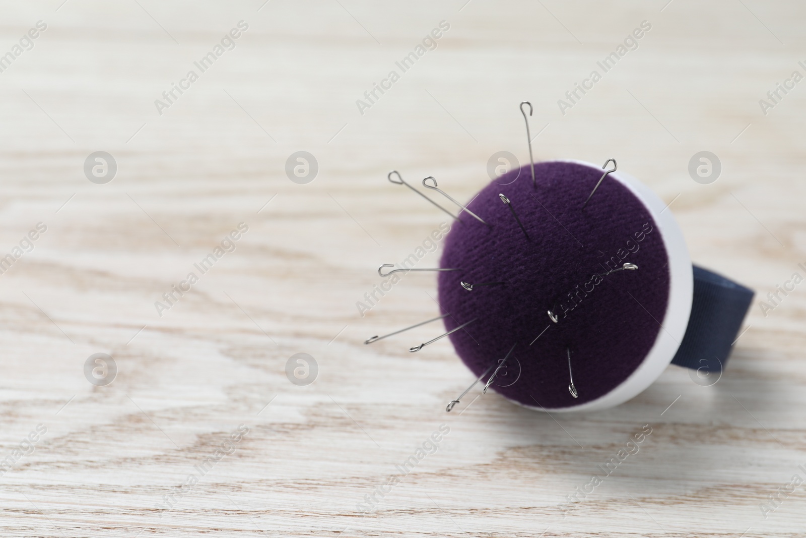 Photo of Blue pincushion with sewing pins on light wooden table. Space for text