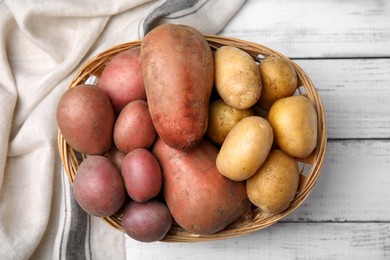 Different types of fresh potatoes in wicker basket on white wooden, flat lay