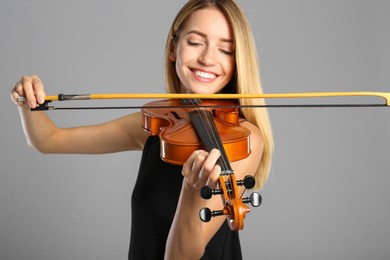 Beautiful woman playing violin on grey background, focus on hand