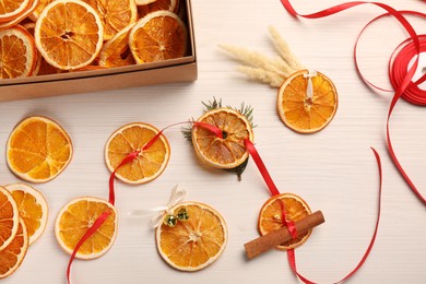 Photo of Beautiful garland with dry oranges, cinnamon, ribbon and sleigh bells on white wooden table, flat lay
