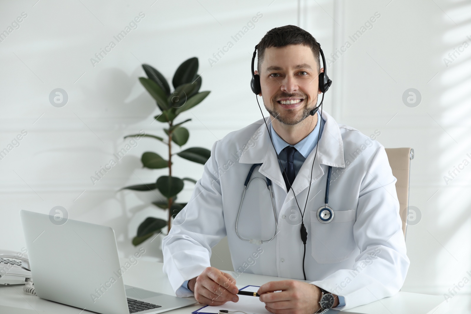 Photo of Doctor with headset sitting at desk in clinic. Health service hotline