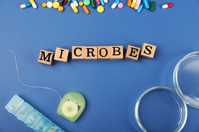 Photo of Word Microbes made with wooden cubes, pills and dental floss on blue background, flat lay