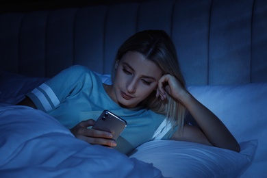 Photo of Young woman using smartphone in bed at night. Nomophobia and sleeping disorder problem