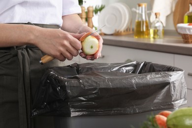 Photo of Woman peeling fresh onion with knife above garbage bin indoors, closeup