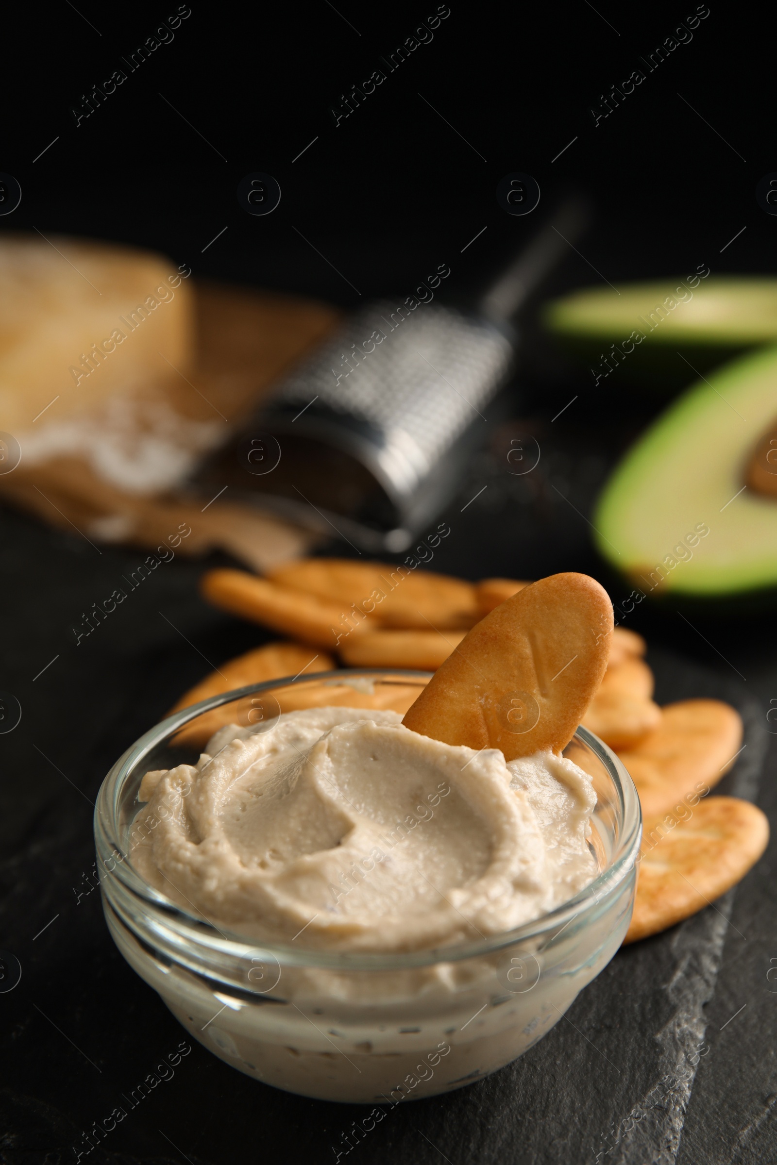 Photo of Delicious crackers and humus on black table, closeup. Space for text