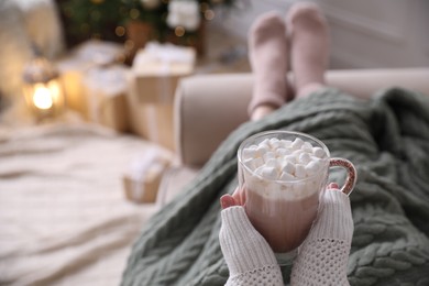 Photo of Woman with delicious hot drink wrapped in plaid on sofa at home, closeup. Space for text