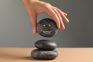 Photo of Woman putting stone with drawn happy face on stack against grey background, closeup. Zen concept
