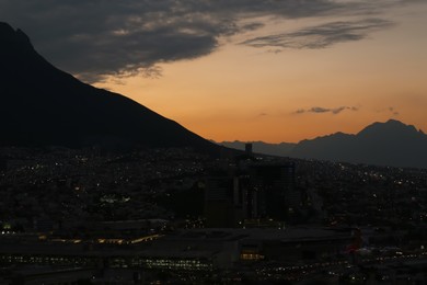 Photo of Picturesque view of sunset with dark clouds above big mountains and evening city