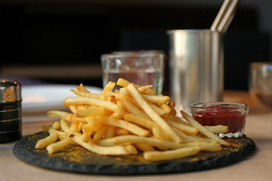 Photo of Tasty French fries with red sauce served on table in cafe