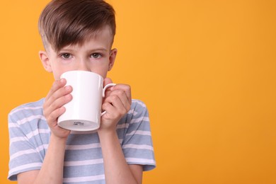 Photo of Cute boy drinking beverage from white ceramic mug on orange background, space for text
