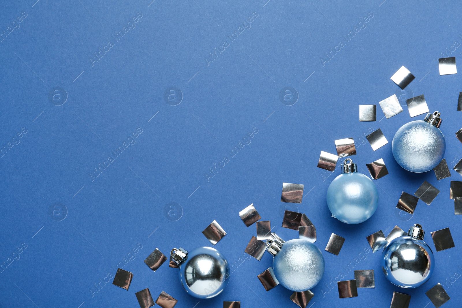 Photo of Flat lay composition with shiny Christmas balls and confetti on blue background, space for text