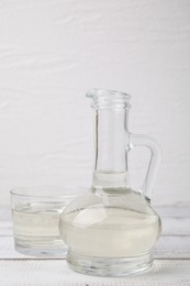 Vinegar in glass jug and bowl on white wooden table