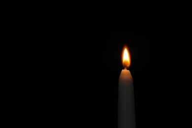 Burning candle on dark background, space for text. Symbol of sorrow