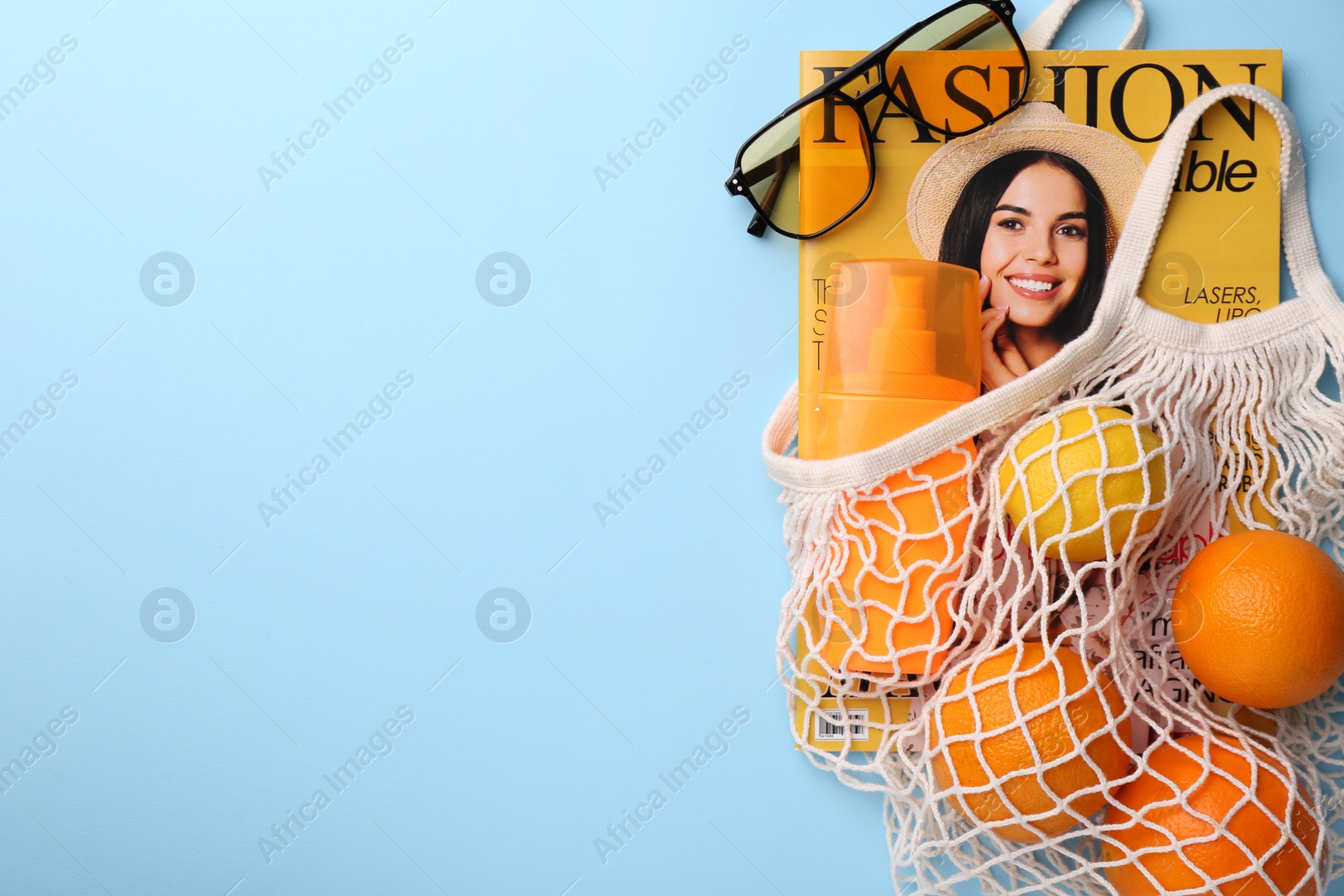 Photo of String bag with magazine, fruits and summer accessories on light blue background, flat lay. Space for text