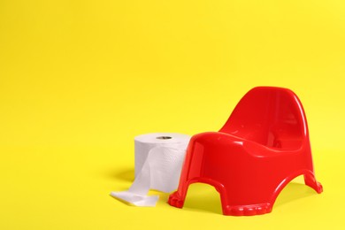 Red baby potty and toilet paper on yellow background, space for text