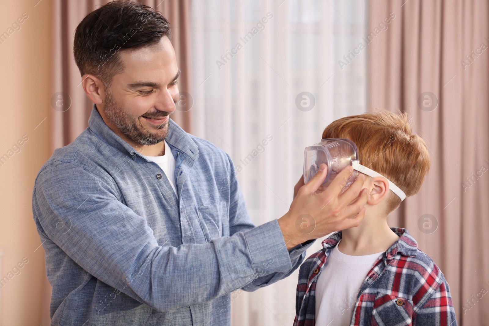 Photo of Father putting protective glasses on his son indoors. Repair work