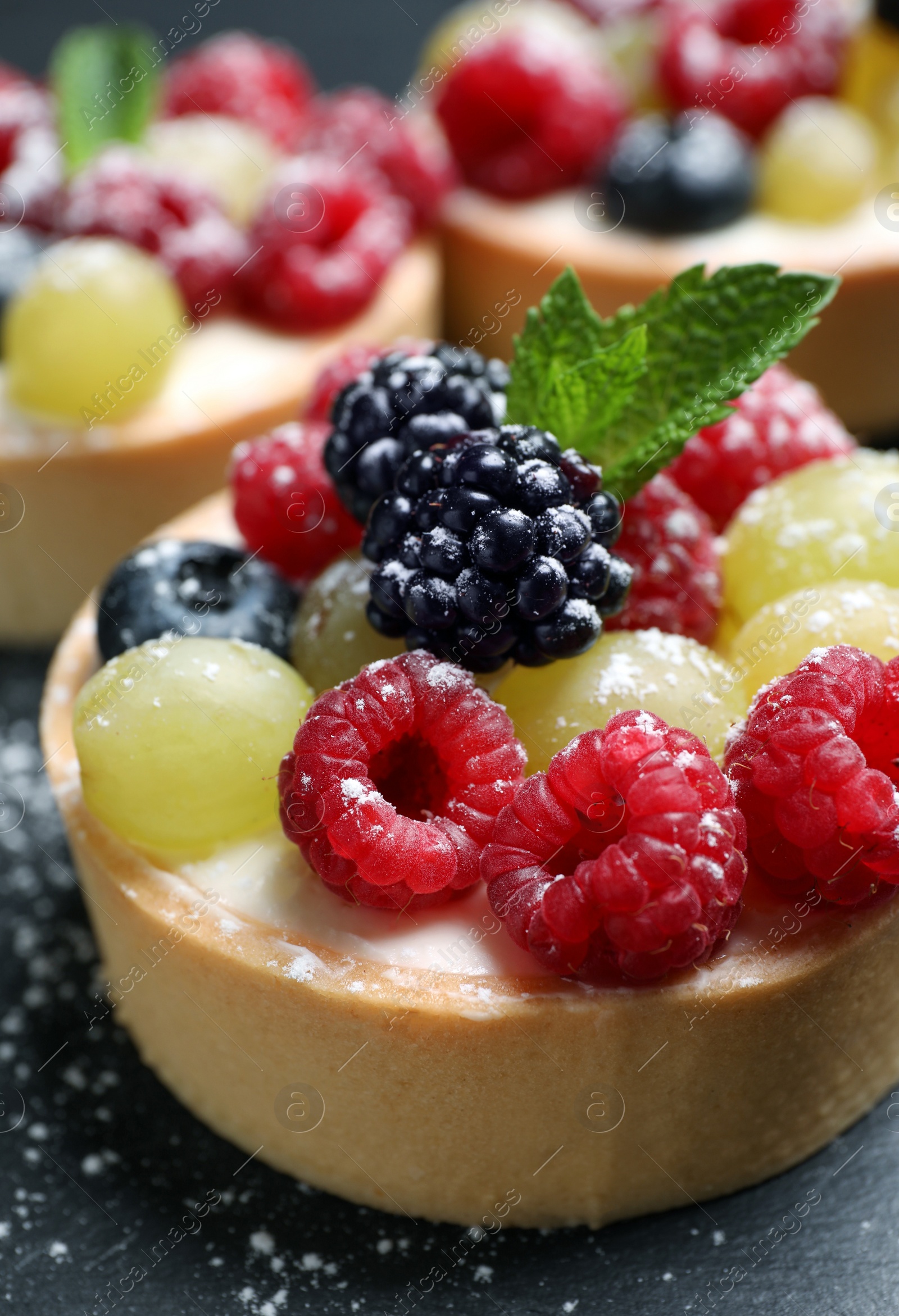 Photo of Delicious tartlets with berries on black table, closeup