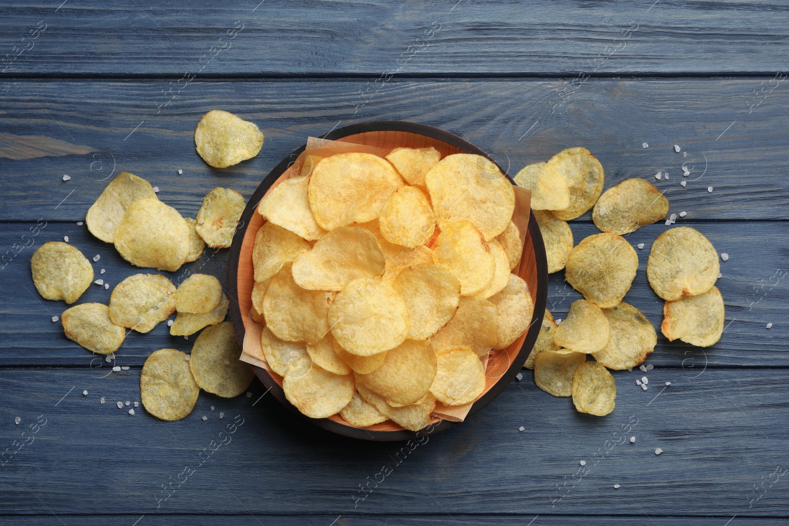 Photo of Bowl and potato chips on wooden table, flat lay