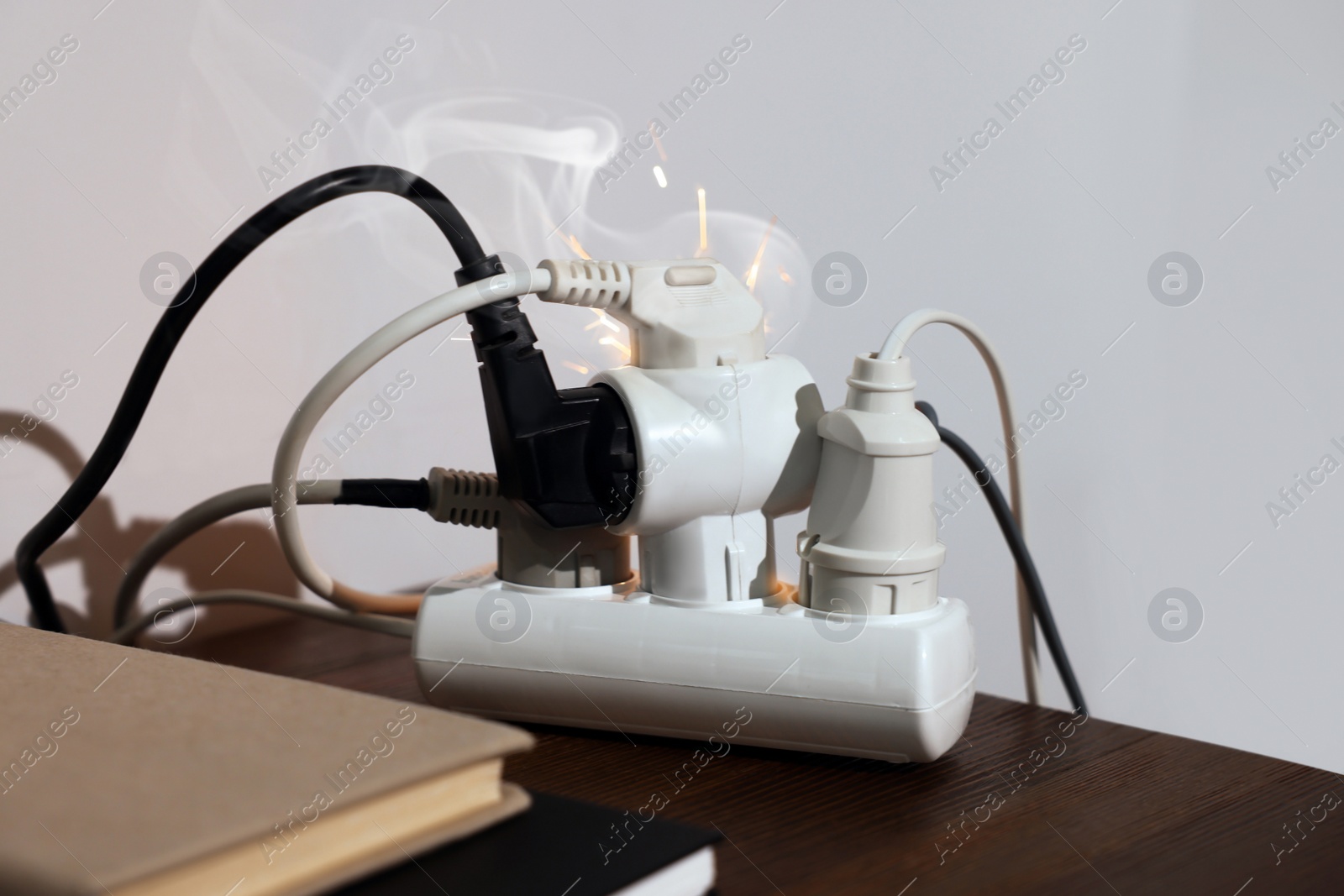 Photo of Inflamed plug in power strip indoors on wooden table. Electrical short circuit