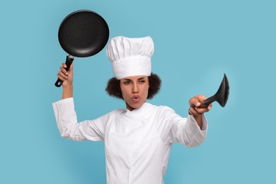 Photo of Female chef with skimmer and frying pan having fun on light blue background