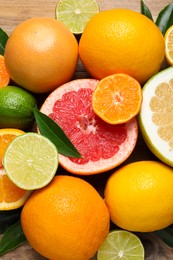 Photo of Different ripe citrus fruits with green leaves on wooden table, flat lay