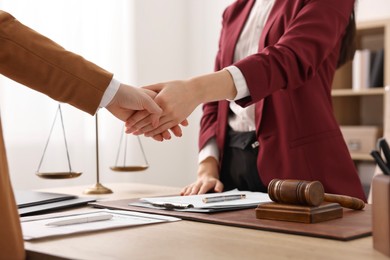 Photo of Notary shaking hands with client at wooden table in office, closeup