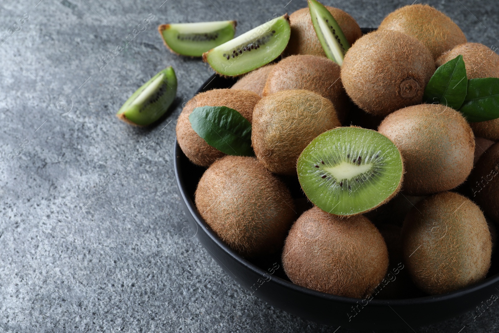 Photo of Fresh ripe kiwis in bowl on grey table, space for text
