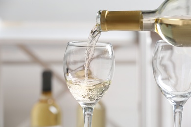 Pouring delicious white wine into glass on light background