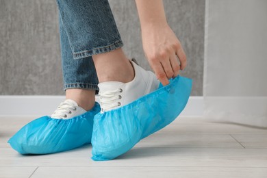 Photo of Woman wearing blue shoe covers onto her sneakers indoors, closeup