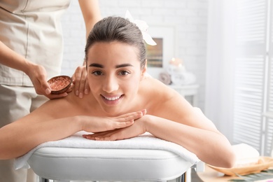 Young woman having body scrubbing procedure with sea salt in spa salon