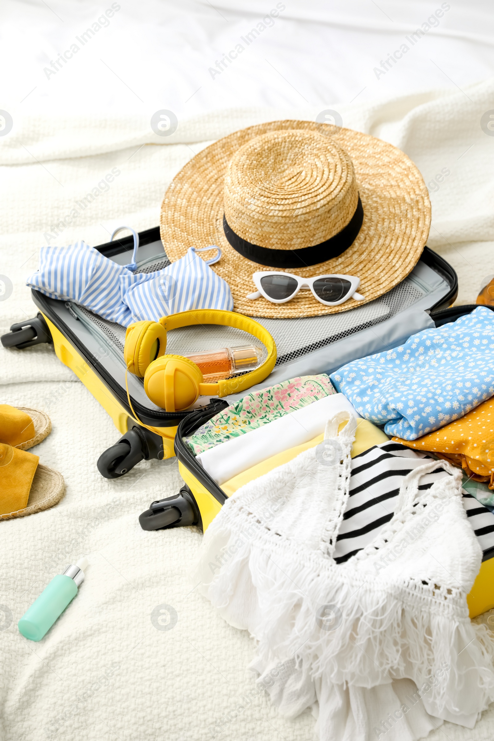 Photo of Open suitcase full of clothes, shoes and summer accessories on bed