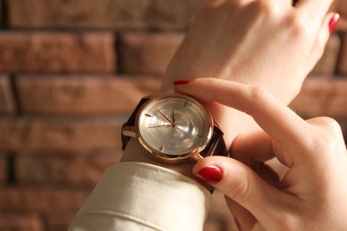 Photo of Woman wearing luxury wristwatch near brick wall, closeup