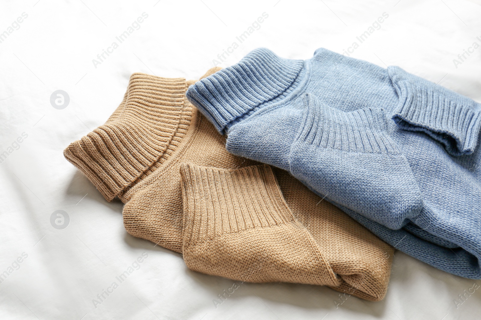 Photo of Stylish soft knitted sweaters on white fabric