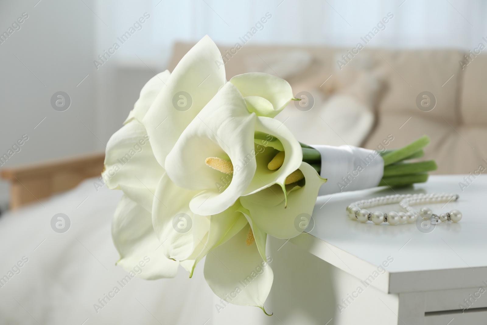 Photo of Beautiful calla lily flowers tied with ribbon and jewelry on white chest of drawers indoors