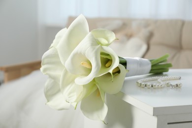 Beautiful calla lily flowers tied with ribbon and jewelry on white chest of drawers indoors