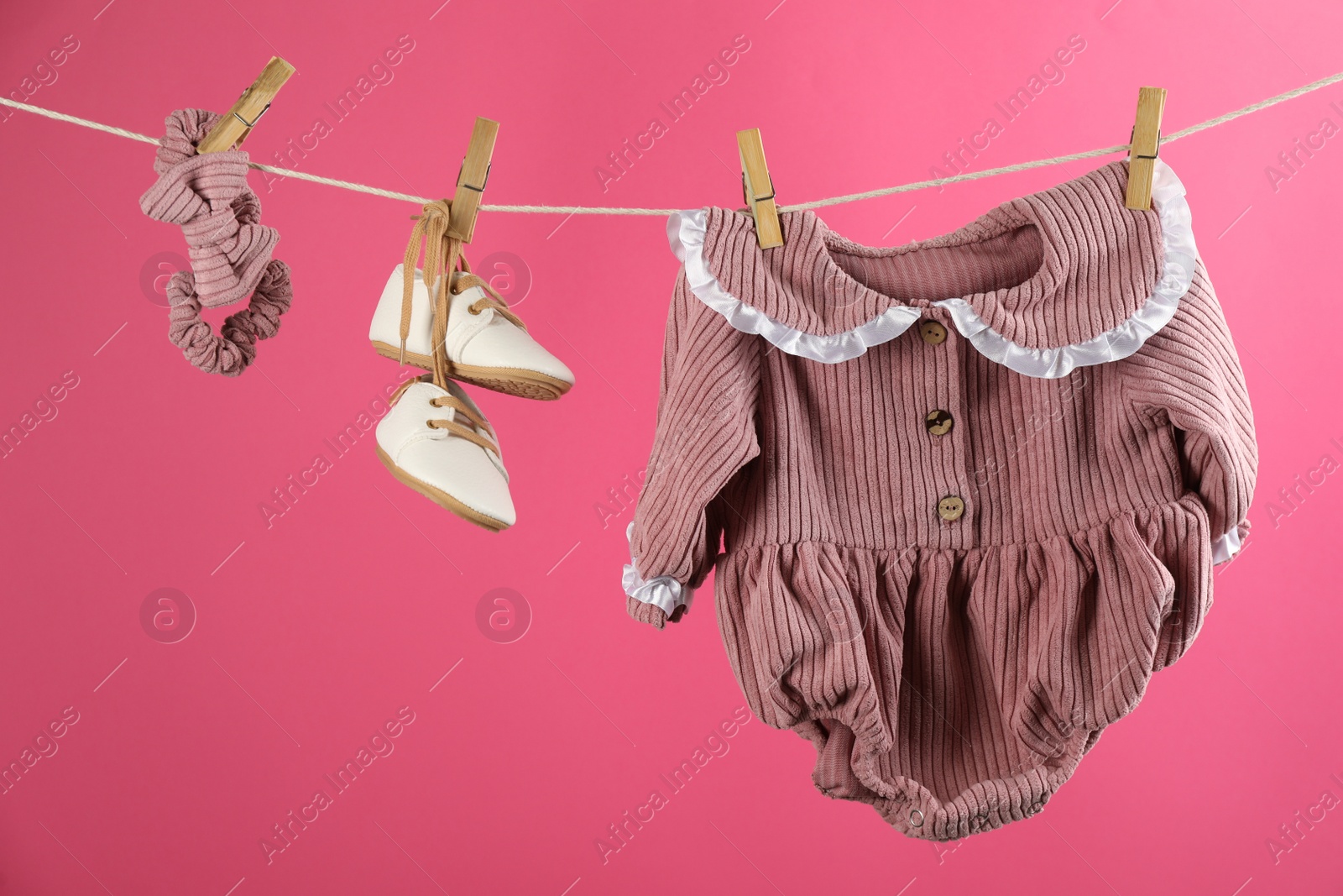 Photo of Baby clothes and accessories hanging on washing line against pink background