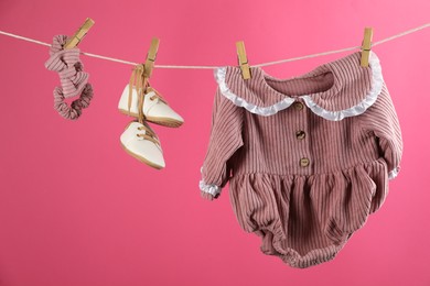 Baby clothes and accessories hanging on washing line against pink background