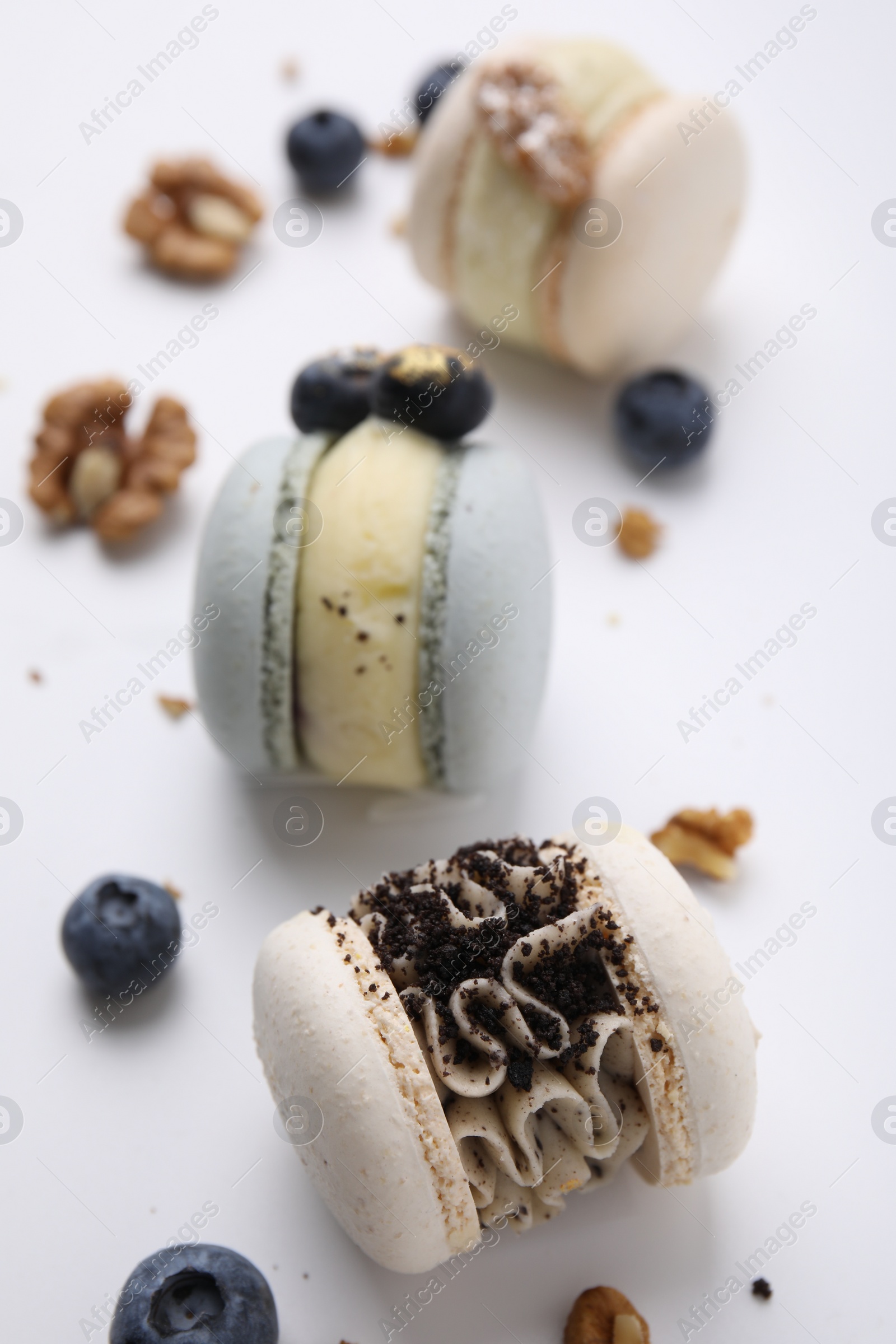 Photo of Delicious macarons, walnuts and blueberries on white table, closeup
