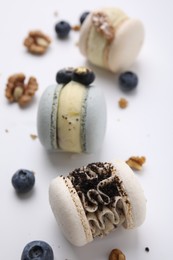 Delicious macarons, walnuts and blueberries on white table, closeup